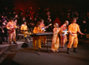 On stage in the orange suits, the crowd in black