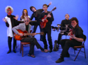 The seven members with painted faces on a blue set
